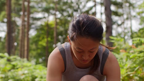 Woman-Kneeling-Down-Tying-Laces-On-Training-Shoe-Before-Exercising-Running-Along-Track-Through-Forest-1